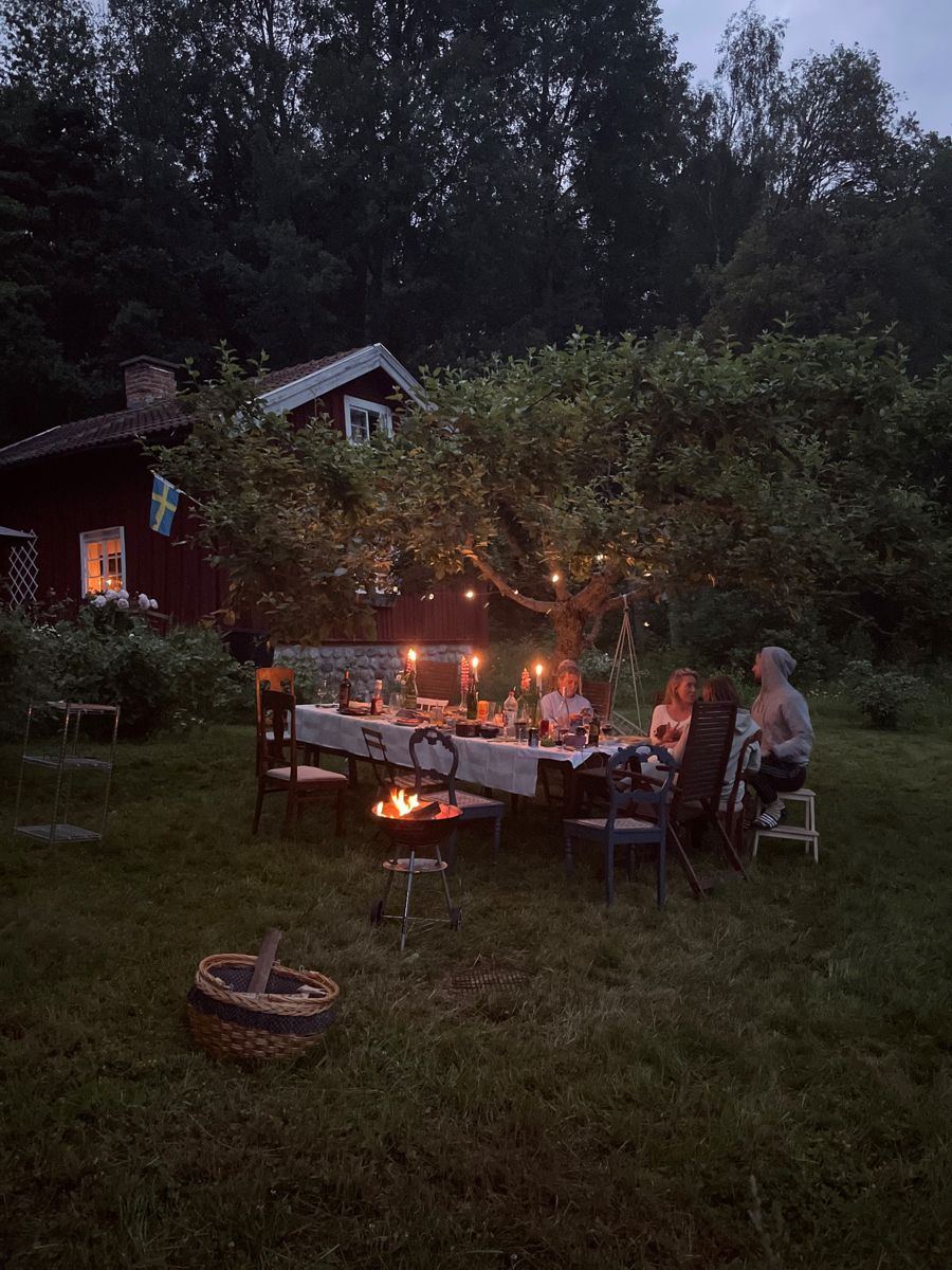 Shared house group dinner at dusk under a tree strung with lights