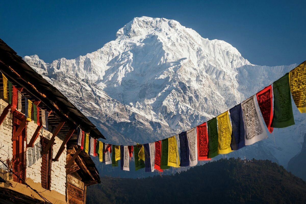 Snow-capped Himalayan peak behind prayer flags and a mountain guesthouse