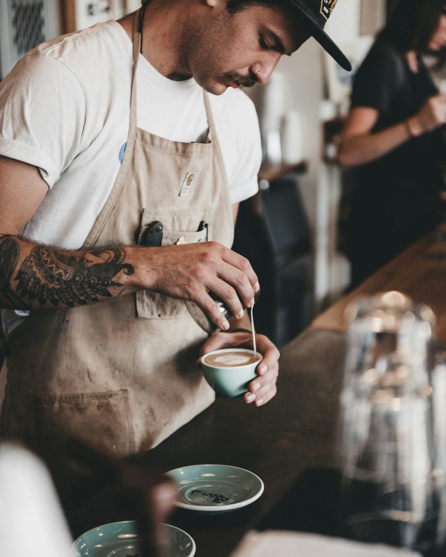 Traveller working as a barista, pouring latte art