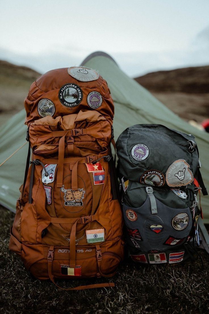 Two backpacks covered in travel patches in front of a tent